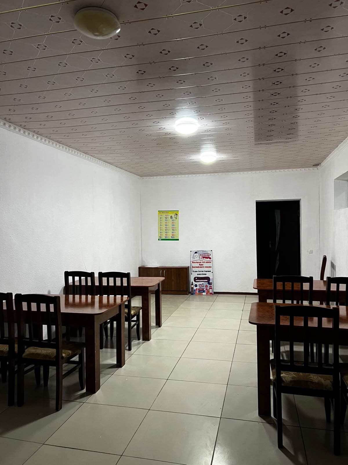 The classroom: wooden tables and chairs, white walls, a numbers poster and a course banner